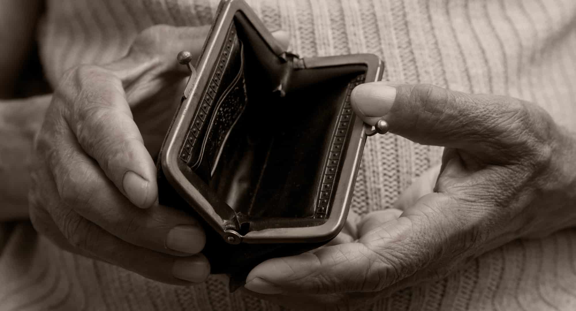 sepia toned image close up of elderly hands holding open an empty money purse.